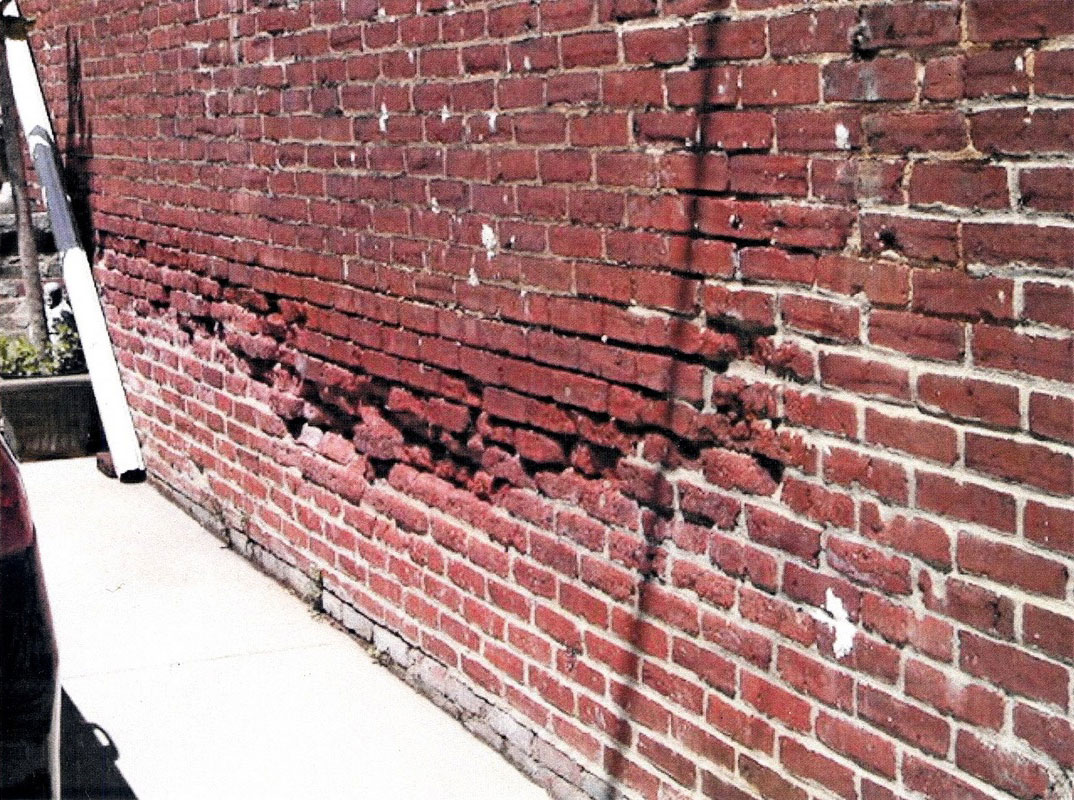 A water-damaged brick wall shows significant damage to the bricks and mortar.